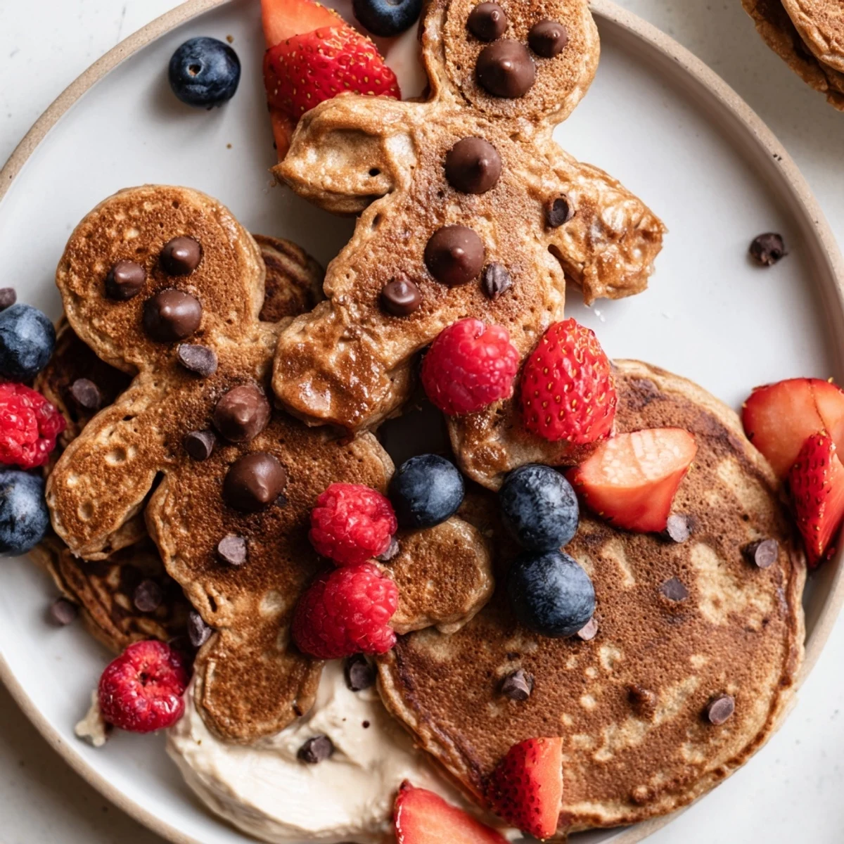 A vibrant Gingerbread Boy Berry Board, featuring golden pancakes, ripe berries, and a dollop of creamy yogurt.