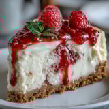 A rich slice of Indulgent White Chocolate Raspberry Cheesecake Bliss, garnished with a fresh raspberry and delicate white chocolate shavings, presenting an elegant dessert perfect for a cozy dinner party.