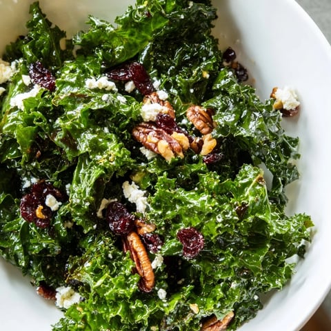 Vibrant massaged kale salad with warm maple-mustard dressing, toasted pecans, dried cranberries, and feta served on a white platter.