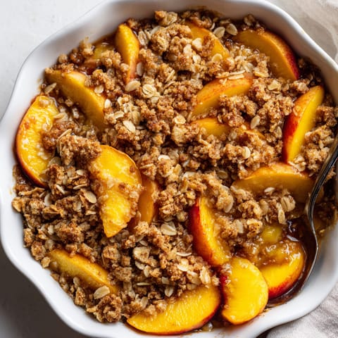 A bowl of peach crisp with oat topping.