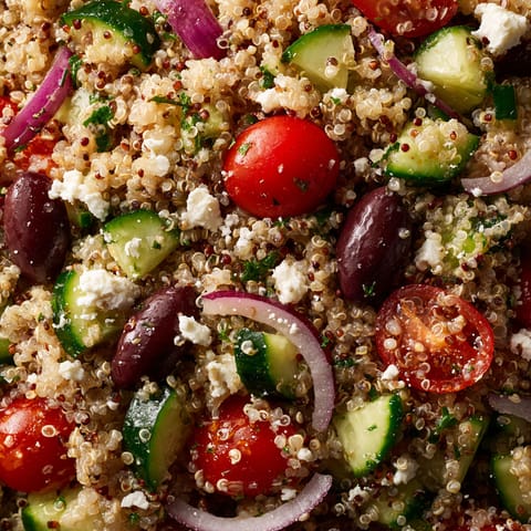 A close up of a salad with tomatoes, cucumbers, onions, and quinoa.