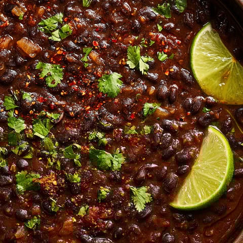 A bowl of spicy black bean soup with lime wedges on top.