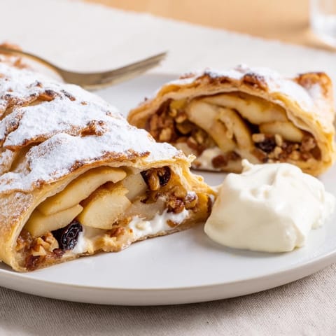 Warm Classic Apple Strudel served with whipped cream and a side of vanilla sauce.  