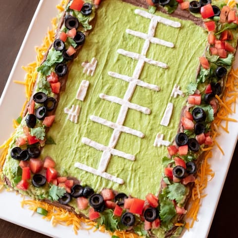 A visually appealing, layered Football Field Dip, featuring a creamy guacamole "field" and colorful toppings.