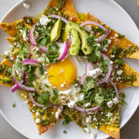 Homemade chilaquiles garnished with red onion, fresh cilantro, and a dollop of sour cream for a vibrant Mexican breakfast.  