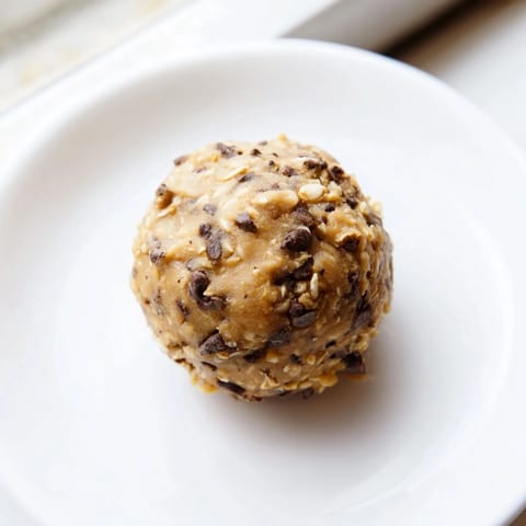 A close-up of homemade Banana Chocolate Chip Energy Balls on a wooden board, showing rolled oats and chocolate chips.