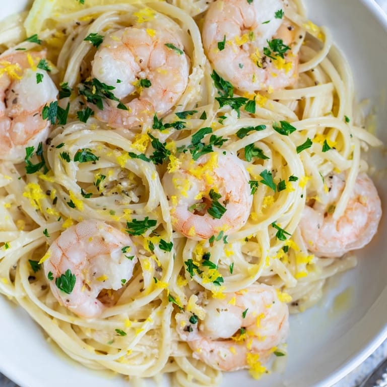 Plated Shrimp Scampi With Linguine brightened by lemon zest and parsley, served with lemon wedges and a glass of white wine.