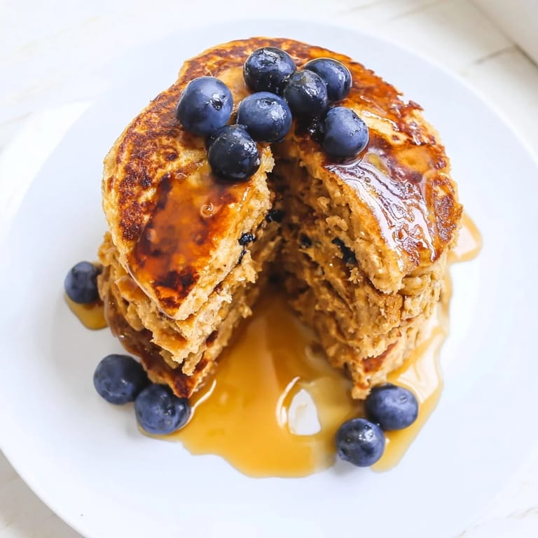 Freshly flipped Banana Oat Pancakes sizzle on a griddle, showcasing their fluffy texture and hearty oat specks.  