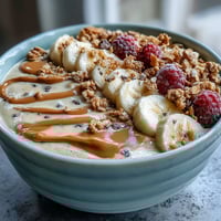 Creamy vegan peanut butter banana protein smoothie bowl topped with fresh berries and crunchy granola for a healthy breakfast.